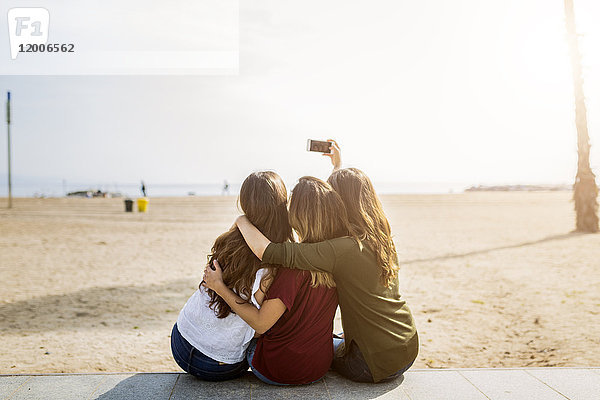 Rückansicht von drei Freundinnen am Strand mit einem Selfie