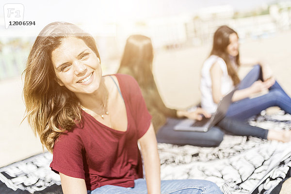 Porträt einer lächelnden jungen Frau am Strand mit Freunden im Hintergrund