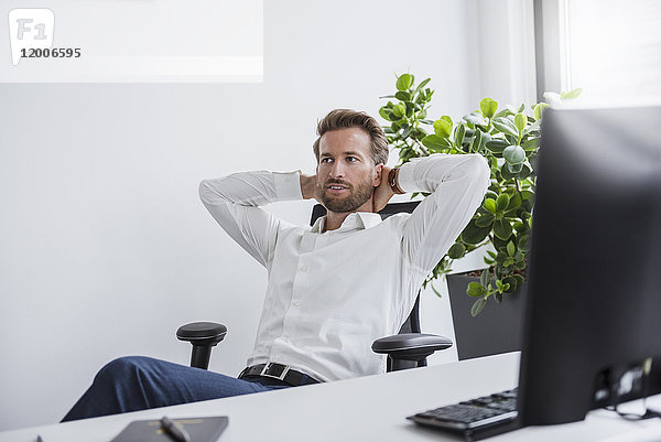 Porträt eines Geschäftsmannes  der sich am Schreibtisch in seinem Büro entspannt.