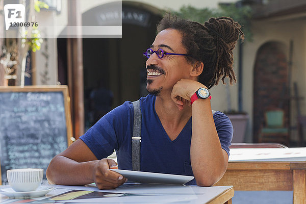 Lächelnder Mann gemischter Rasse  der ein digitales Tablet in einem Straßencafé benutzt