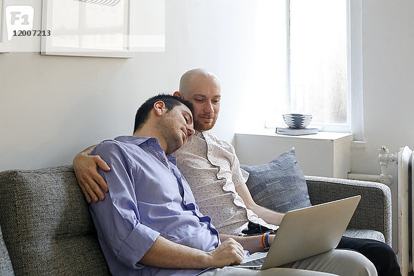 Kaukasische Männer  die sich auf dem Sofa umarmen und einen Laptop benutzen