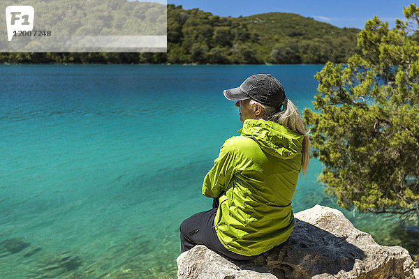 Kaukasische Frau sitzt auf einem Felsen am See