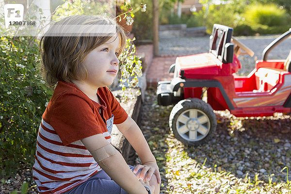 Nachdenklicher kaukasischer Junge sitzt in der Nähe eines Spielzeugautos