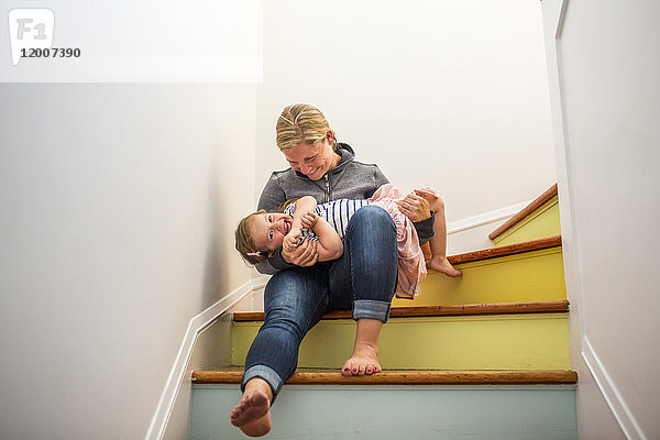 Kaukasische Mutter und Tochter spielen auf einer mehrfarbigen Treppe