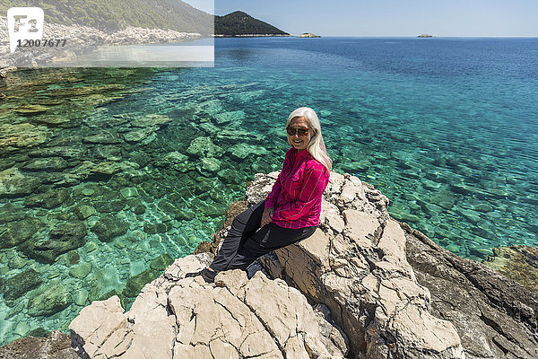 Kaukasische Frau posiert auf einem Felsen am See