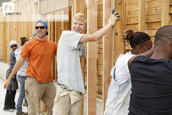 Lächelnde Freiwillige halten eine gerahmte Wand auf der Baustelle