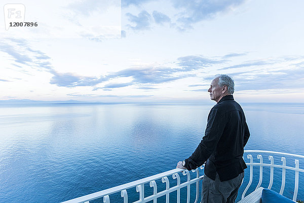 Kaukasischer Mann bewundert die Aussicht auf einem Balkon am Wasser