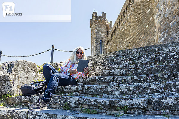 Kaukasische Frau  die auf einer Treppe sitzt und ein digitales Tablet liest