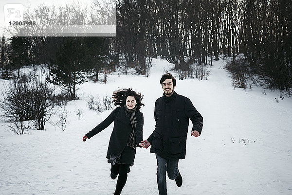 Kaukasisches Paar rennt im Winter aus dem Wald