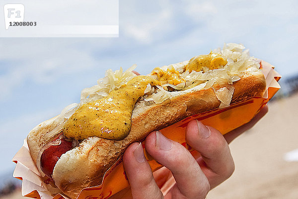 Hot Dog mit Senf und Sauerkraut in der Hand