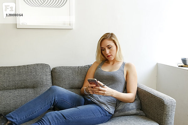 Kaukasische Frau sitzt auf dem Sofa und schreibt eine SMS auf ihrem Handy