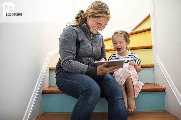 Kaukasische Mutter und Tochter benutzen ein digitales Tablet auf einer Treppe