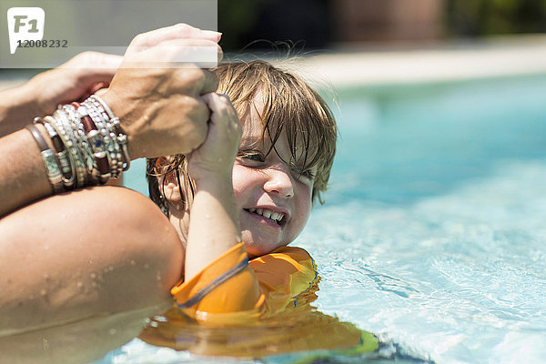 Kaukasische Mutter hält die Hände eines schwimmenden Jungen