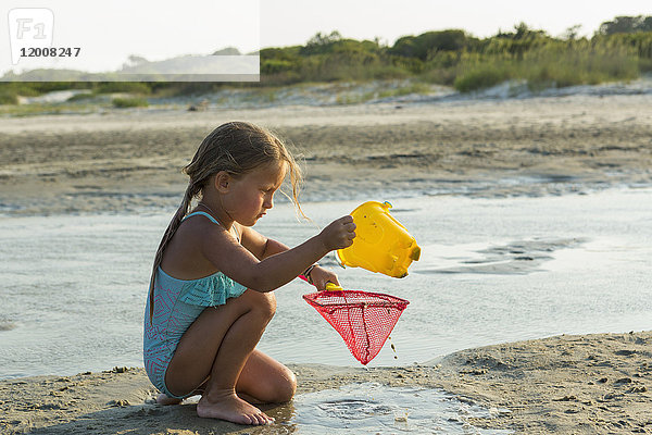 Kaukasisches Mädchen  das am Strand kniet und Wasser in ein Netz gießt