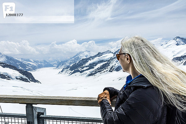 Kaukasische Frau lehnt sich an ein Geländer und bewundert die schöne Aussicht auf die Berge
