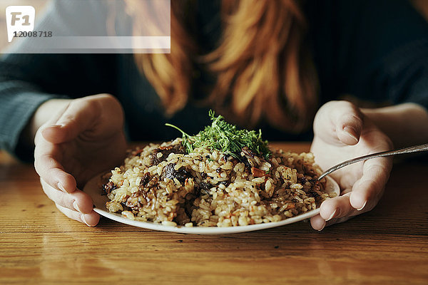 Die Hände einer Frau halten einen Teller mit Reis