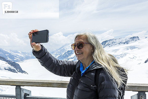 Kaukasische Frau posiert für Handy-Selfie in der Nähe von verschneiten Bergen