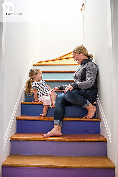 Kaukasische Mutter und Tochter lachend auf mehrfarbiger Treppe