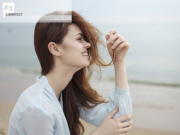 Lächelnde Frau mit Haaren am Strand sitzend