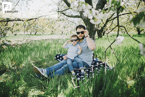 Kaukasischer Vater und Sohn mit Sonnenbrille auf einer Decke im Gras