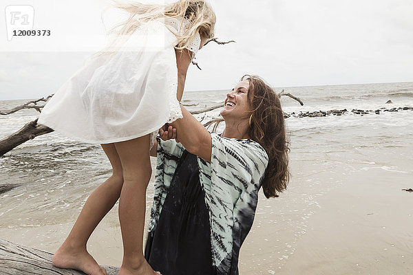 Kaukasische Mutter und Tochter spielen auf Treibholz am Strand