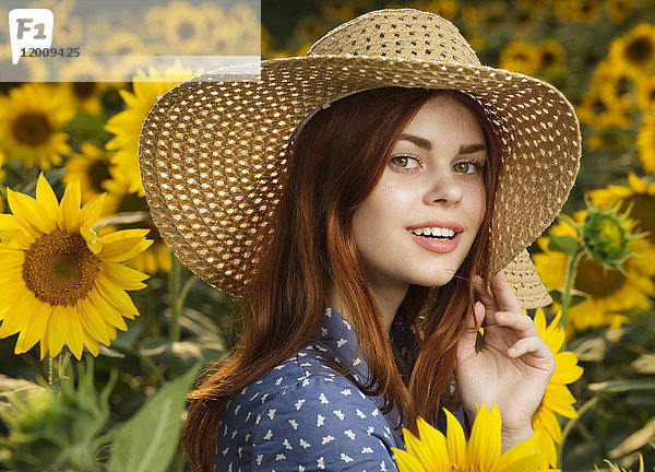 Lächelnde kaukasische Frau mit Hut in einem Sonnenblumenfeld