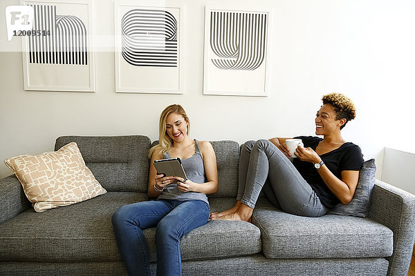 Frauen trinken Kaffee und benutzen ein digitales Tablet auf dem Sofa