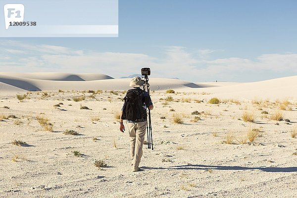 Rückansicht eines kaukasischen Fotografen mit Stativ in der Wüste