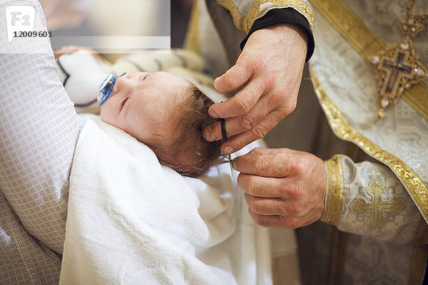 Priester schneidet die Haare eines kleinen Mädchens