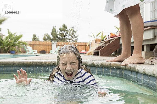 Kaukasischer Junge gießt Wasser auf seine Schwester im Schwimmbad