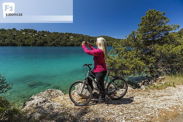 Kaukasische Frau auf dem Fahrrad fotografiert See mit Handy