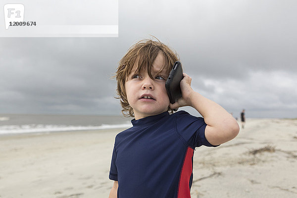 Kaukasischer Junge  der am Strand mit einem Handy telefoniert