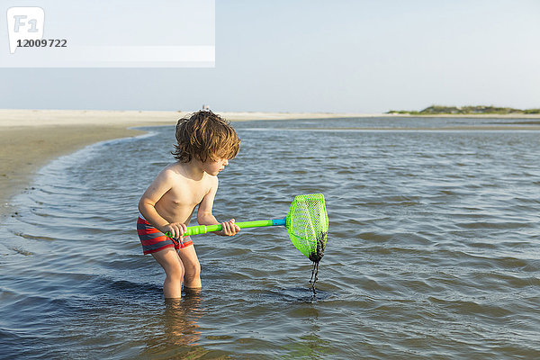 Kaukasischer Junge watet im Meer und hält