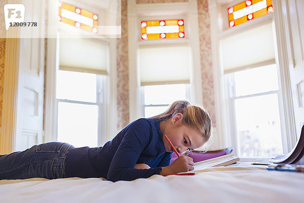 Kaukasisches Mädchen liegt auf dem Bett und schreibt in ein Notizbuch