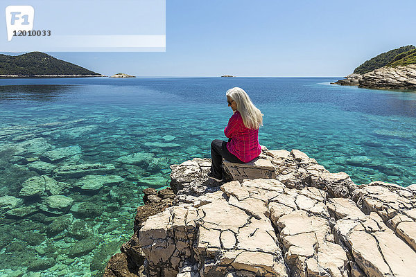 Kaukasische Frau sitzt auf einem Felsen und bewundert den See