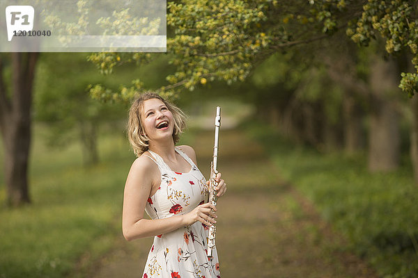Kaukasisches Teenager-Mädchen hält Flöte im Park und lacht
