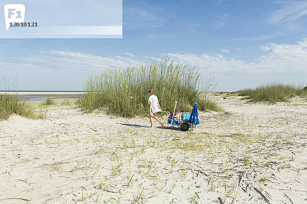 Kaukasische Mutter  die ihren Sohn in einem Wagen am Strand zieht