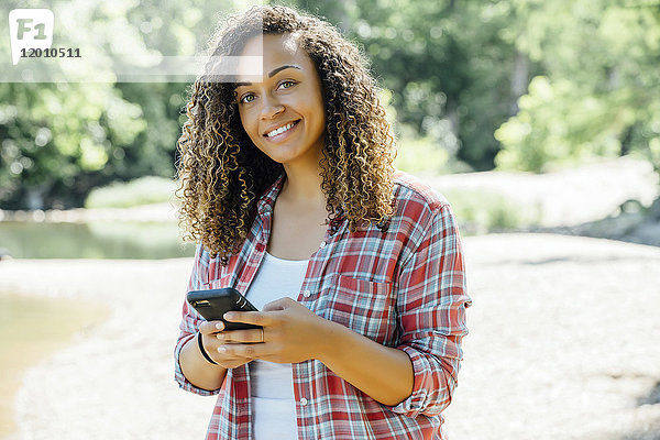 Lächelnde gemischtrassige Frau  die im Freien eine SMS auf ihrem Handy schreibt
