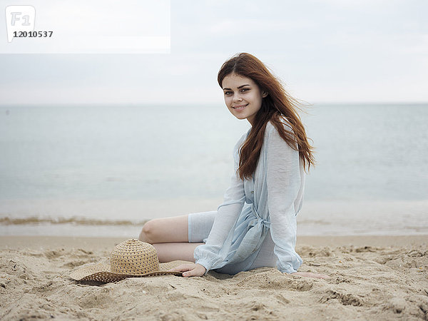 Lächelnde kaukasische Frau sitzt am Strand