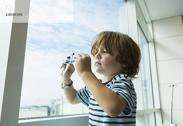 Kaukasischer Junge spielt mit Spielzeugflugzeug in der Nähe des Fensters