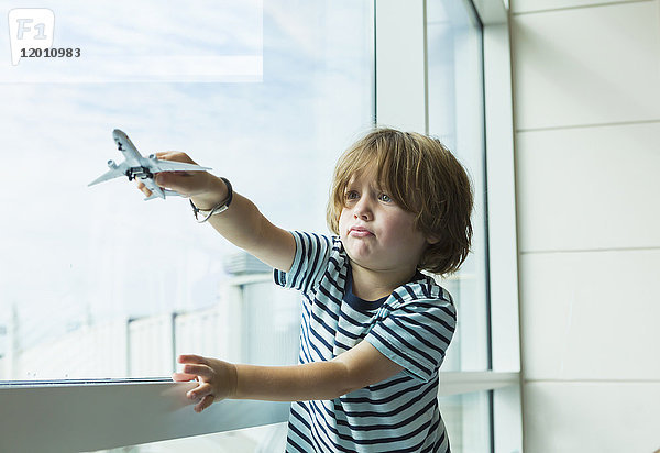 Kaukasischer Junge spielt mit Spielzeugflugzeug in der Nähe des Fensters