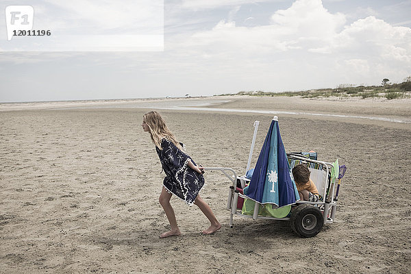 Mädchen  das seinen Bruder in einem Wagen am Strand zieht