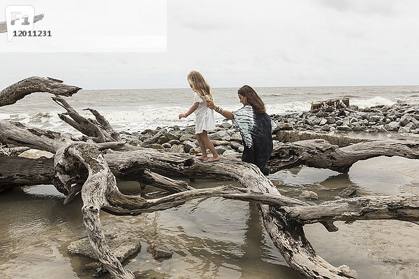 Kaukasische Mutter und Tochter gehen am Strand auf Treibholz