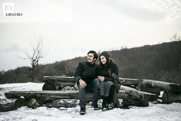 Kaukasisches Paar sitzt im Winter auf Baumstämmen