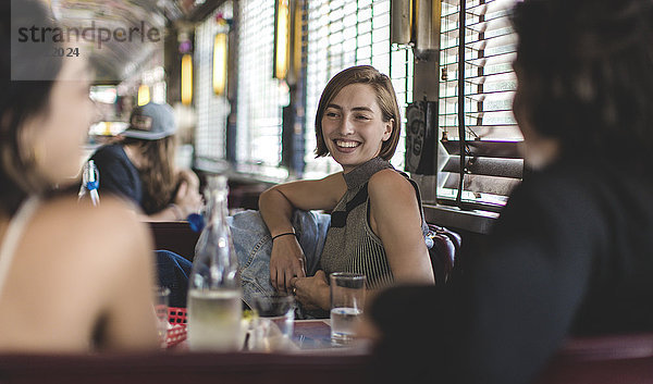 Lächelnde Frau  die mit zwei Freunden in einer Kabine in einem Diner sitzt.