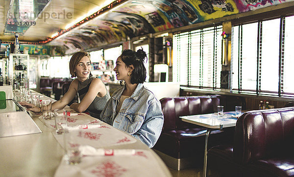 Zwei junge Frauen sitzen nebeneinander an einer Theke in einem Diner.