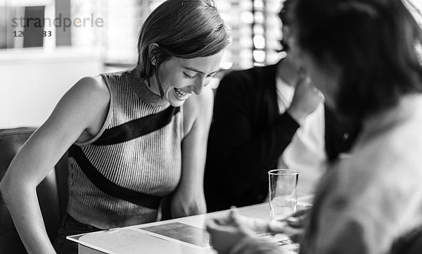 Lächelnde Frau  die mit zwei Freunden in einer Kabine in einem Diner sitzt und nach unten schaut.