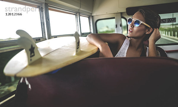 Junge Frau  die mit einem Surfbrett in einem Bus sitzt.