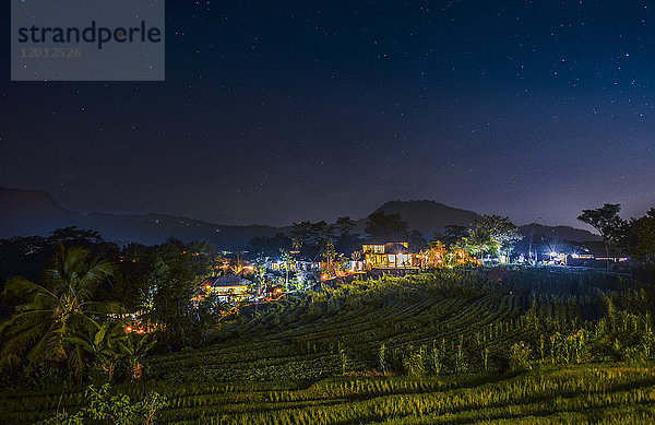 Nachtansicht der Insel Bali  Blick über Felder und Hänge  auf ein beleuchtetes Dorf.