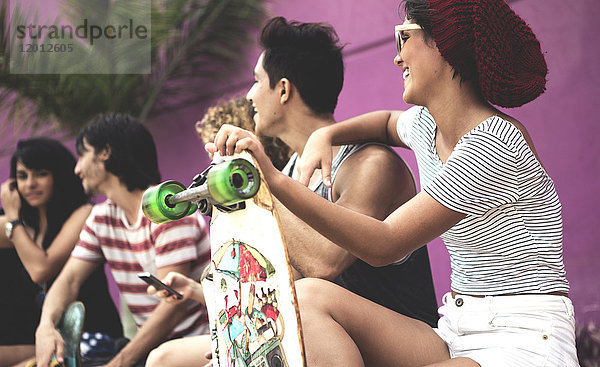 Eine Gruppe junger Leute sitzt  einer hält ein Skateboard in der Hand.